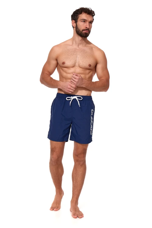 Granatowe długie szorty kąpielowe męskie ZAGANO 5115 LONG-NAVY BLUE z białym sznurkiem do regulacji i dużym pionowym logo marki na nogawce. Wygodny, sportowy fason z bocznymi kieszeniami i tylną kieszenią z klapką, idealny na basen, plażę i do pływania.